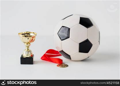 sport, achievement, championship, competition and success concept - close up of football or soccer ball with golden medal and cup over white background