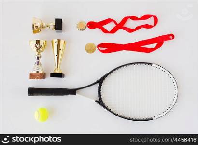 sport, achievement, championship, competition and success concept - close up of tennis racket and ball with cups and medals over white background