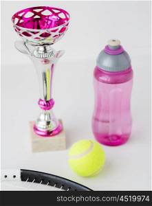 sport, achievement, championship, competition and success concept - close up of tennis racket and ball with cup and bottle over white background