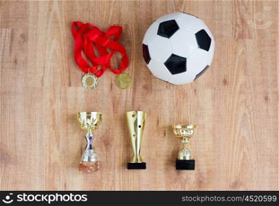 sport, achievement, championship, competition and success concept - football or soccer ball with golden medals and cups over wooden background