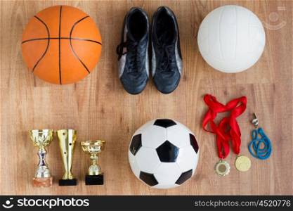 sport, achievement, success and competition concept - different balls, boots with golden cups, whistle and medals over wooden background