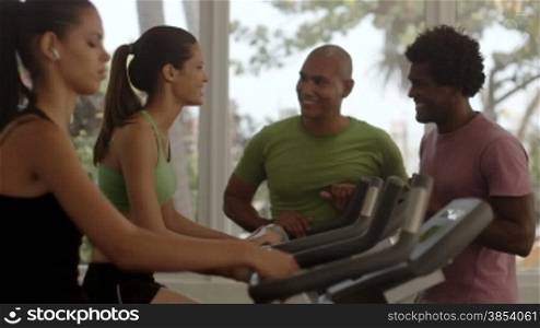 Sport and fun, young men and women talking and laughing in gym while working out and exercising on bike