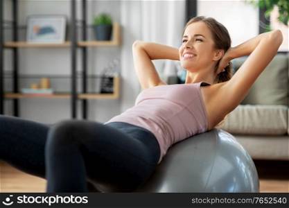 sport and healthy lifestyle concept - happy woman exercising on fitness ball at home. happy woman exercising on fitness ball at home