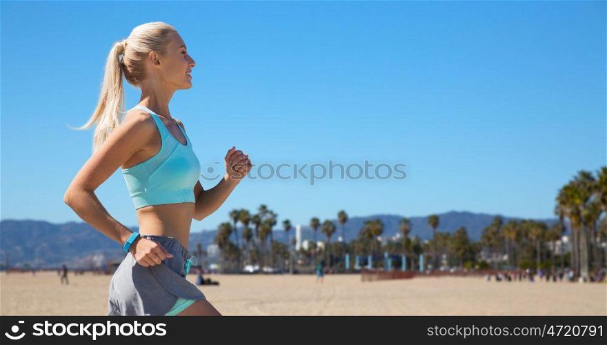 sport and healthy lifestyle concept - smiling young woman with fitness tracker running over venice beach background in california. woman with fitness tracker running. woman with fitness tracker running