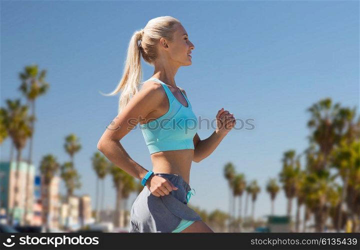 sport and healthy lifestyle concept - smiling young woman with fitness tracker running over venice beach background in california. woman with fitness tracker running. woman with fitness tracker running