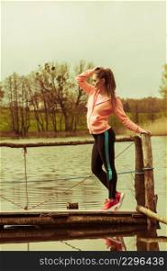 Sport and lifestyle concept. Young sports woman female jogger taking a break from running workout, relaxing on pier on sunny day. Young sports woman taking break after a run.