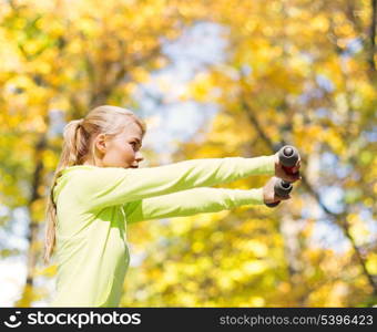 sport and lifestyle concept - young sporty woman with light dumbbells outdoors