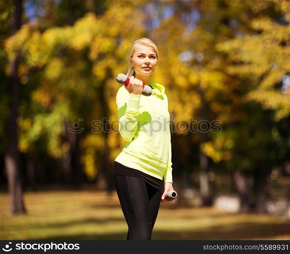 sport and lifestyle concept - young sporty woman with light dumbbells outdoors