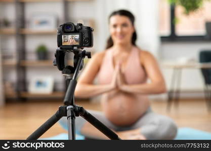 sport and people concept - close up of happy pregnant woman or blogger with camera on tripod recording online yoga class at home. pregnant woman or yoga blogger with camera at home