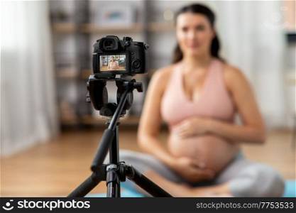sport and people concept - close up of happy pregnant woman or blogger with camera on tripod recording online yoga class at home. pregnant woman or yoga blogger with camera at home