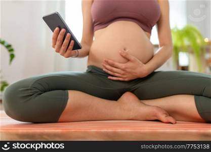 sport and people concept - close up of pregnant woman with smartphone doing yoga at home. close up of pregnant woman with phone doing yoga