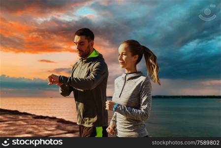 sport and people concept - happy couple with fitness trackers running over sea and sunset sky on background. couple with fitness trackers running over sea