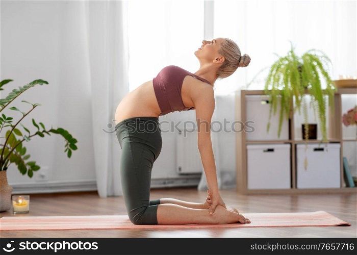 sport and people concept - happy pregnant woman doing yoga camel pose at home. happy pregnant woman doing yoga at home