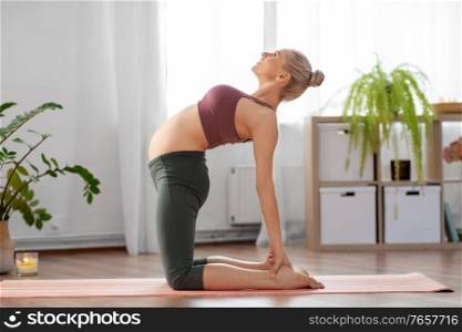 sport and people concept - happy pregnant woman doing yoga camel pose at home. happy pregnant woman doing yoga at home