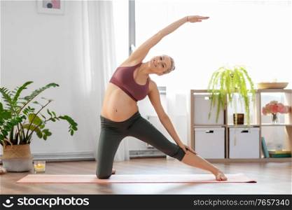 sport and people concept - happy pregnant woman doing yoga gate pose on mat at home. happy pregnant woman doing yoga at home