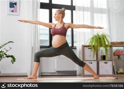 sport and people concept - happy pregnant woman doing yoga warrior pose at home. happy pregnant woman doing yoga at home