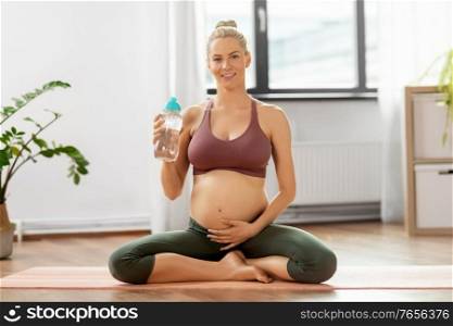 sport and people concept - happy pregnant woman drinking water from bottle after yoga at home. pregnant woman drinking water after yoga at home