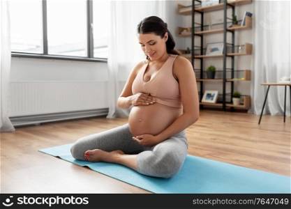 sport and people concept - happy pregnant woman sitting on yoga mat at home. happy pregnant woman sitting on yoga mat at home