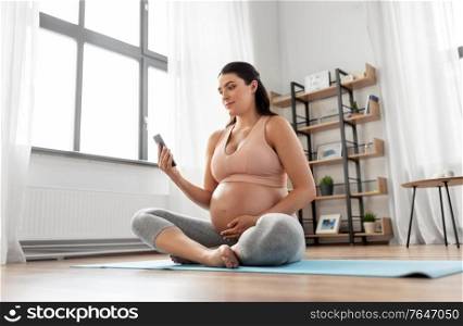 sport and people concept - happy pregnant woman with smartphone doing yoga at home. happy pregnant woman with phone doing yoga at home
