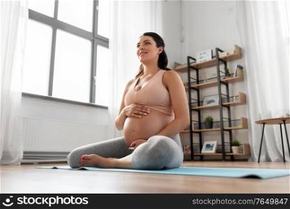 sport and people concept - happy smiling pregnant woman sitting on yoga mat at home. happy pregnant woman sitting on yoga mat at home