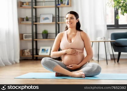 sport and people concept - happy smiling pregnant woman sitting on yoga mat at home. happy pregnant woman sitting on yoga mat at home