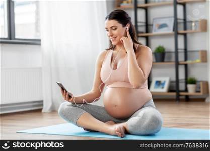 sport and people concept - happy smiling pregnant woman with earphones and smartphone doing yoga at home. pregnant woman with earphones doing yoga at home