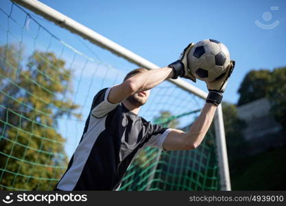 sport and people - soccer player or goalkeeper catching ball at football goal on field. goalkeeper with ball at football goal on field