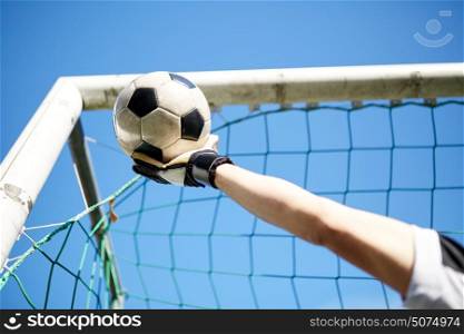 sport and people - soccer player or goalkeeper hand catching ball at football goal over blue sky. goalkeeper with ball at football goal over sky
