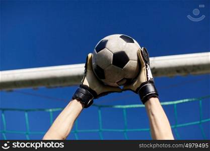 sport and people - soccer player or goalkeeper hands catching ball at football goal over blue sky. goalkeeper with ball at football goal over sky