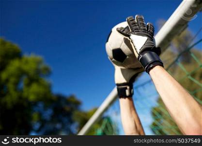 sport and people - soccer player or goalkeeper hands catching ball at football goal on field. goalkeeper with ball at football goal on field