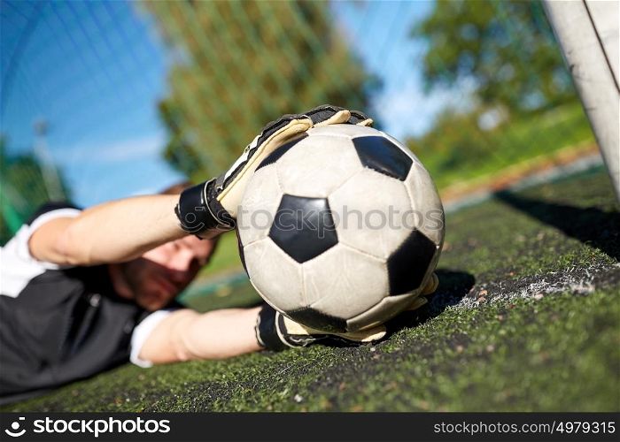 sport and people - soccer player or goalkeeper lying with ball at football goal on field. goalkeeper with ball at football goal on field