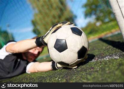 sport and people - soccer player or goalkeeper lying with ball at football goal on field. goalkeeper with ball at football goal on field