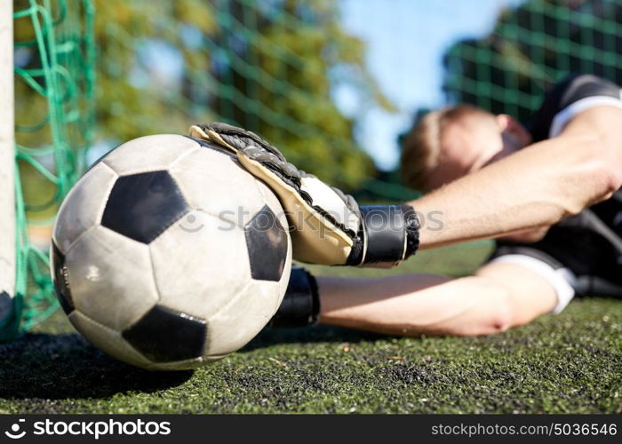 sport and people - soccer player or goalkeeper lying with ball at football goal on field. goalkeeper with ball at football goal on field