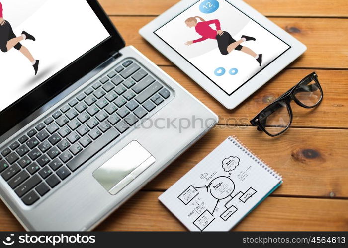 sport and technology concept - close up of on laptop computer and tablet pc with fitness application on screens, notebook and eyeglasses on wooden table