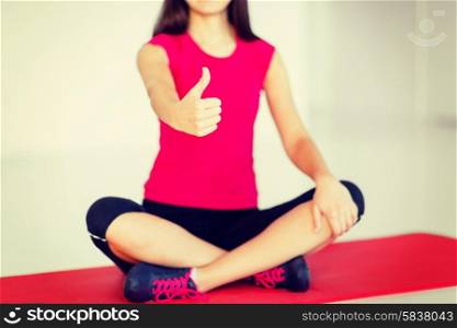 sport and yoga concept - girl sitting in lotus position and showing thumbs up