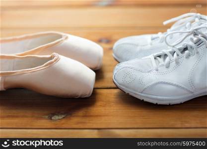 sport, ballet, fitness, footwear and objects concept - close up of sneakers and pointe shoes on wooden floor