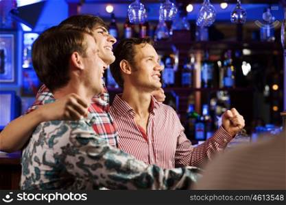 Sport bar. Three young men at bar watching match and shouting