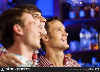 Sport bar. Three young men at bar watching match and shouting