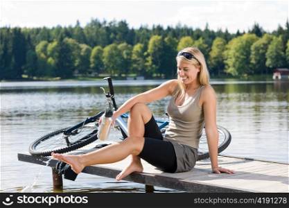 Sport biking young woman sitting on pier by natural lake