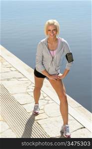 Sport blond woman stretching legs on a pier sunny day
