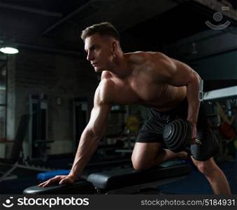sport, bodybuilding, fitness and people concept - young man with dumbbell and bench flexing muscles in gym. man with dumbbell and bench exercising in gym