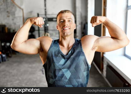 sport, bodybuilding, fitness and power concept - happy smiling young man showing his bicep muscles in gym. happy young man showing his bicep muscles in gym