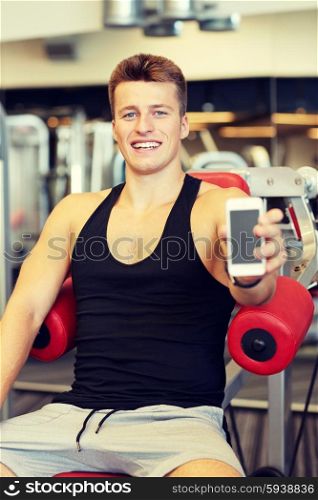 sport, bodybuilding, lifestyle, technology and people concept - smiling young man showing smartphone blank screen in gym