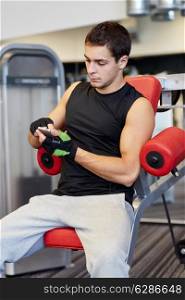 sport, bodybuilding, lifestyle, technology and people concept - young man with smartphone in gym