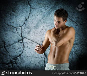 sport, bodybuilding, medicine and people concept - young man applying pain relief gel on his shoulder over concrete wall background