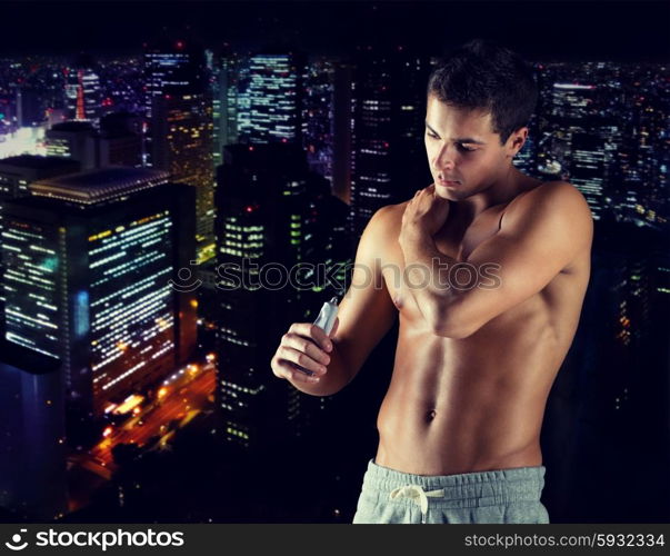 sport, bodybuilding, medicine and people concept - young man applying pain relief gel on his shoulder over concrete wall background