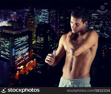 sport, bodybuilding, medicine and people concept - young man applying pain relief gel on his shoulder over concrete wall background