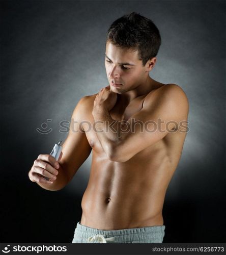 sport, bodybuilding, medicine and people concept - young man standing over black background and applying pain relief gel on his shoulder
