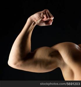 sport, bodybuilding, strength and people concept - close up of young man showing biceps over black background