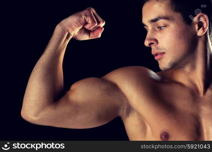 sport, bodybuilding, strength and people concept - close up of young man showing biceps over black background